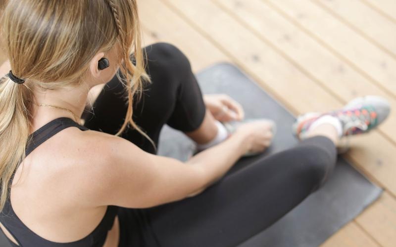 woman in workout gear, sits on a yoga mat and ties her shoe